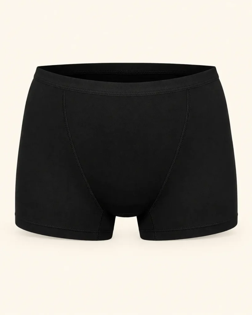 Bóxer menstrual negro de piernas cortas y cintura elástica sobre fondo crema.