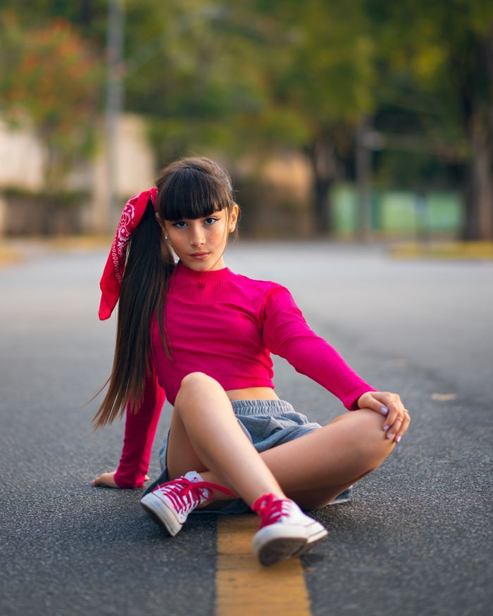 A young girl sits stylishly in the middle of the street, wearing a hot pink shirt.