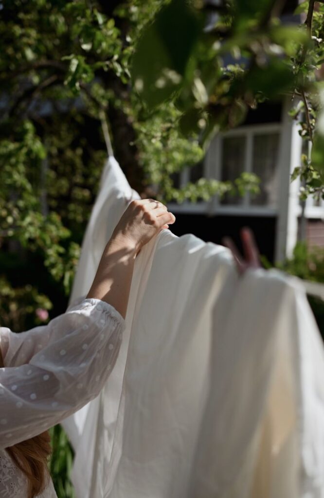 Close-up of a woman hanging a white bed sheet outdoors, capturing the essence of summer laundry day.