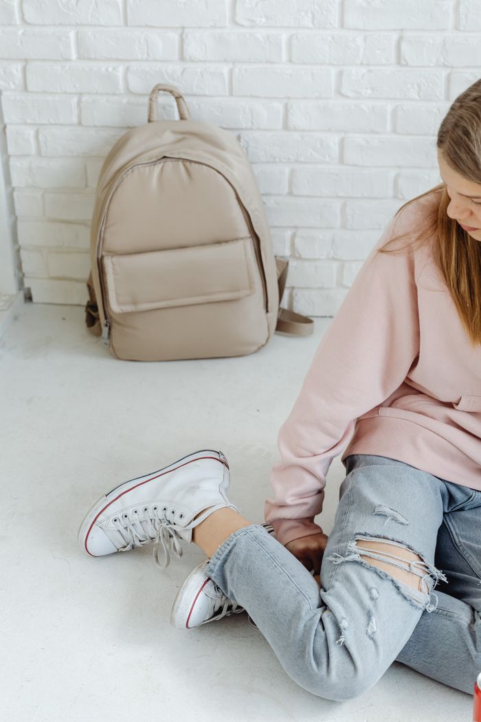 Teenager sitting on the floor in casual attire next to a backpack, perfect for school or lifestyle themes.