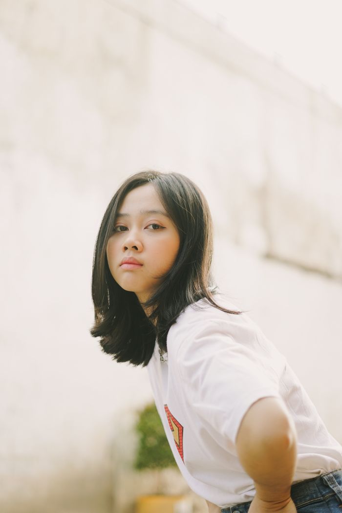 Close-up portrait of an Asian girl in a white shirt posing outside with a soft background.